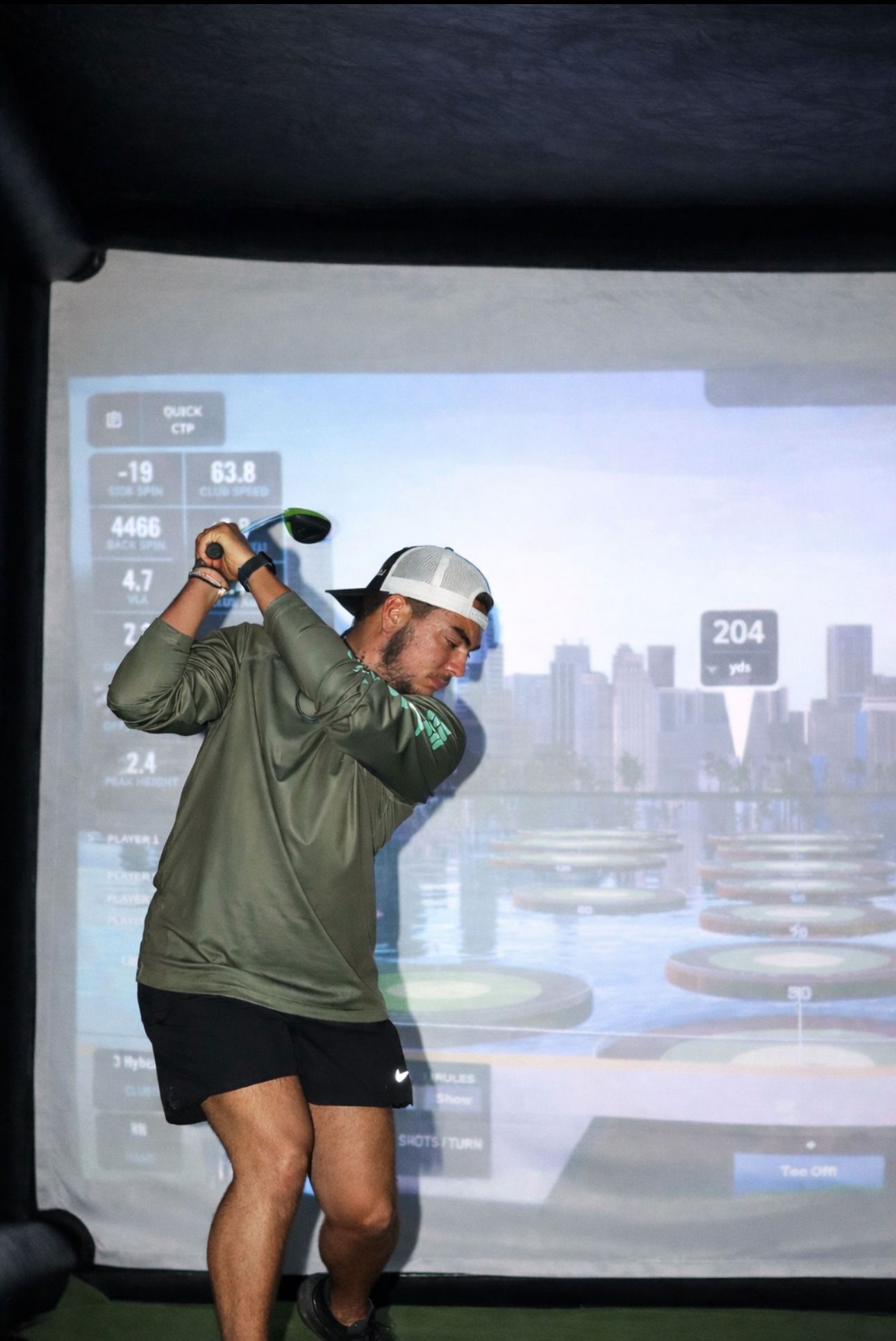 Guest mid-swing inside a PopGolf simulator playing a Miami skyline course